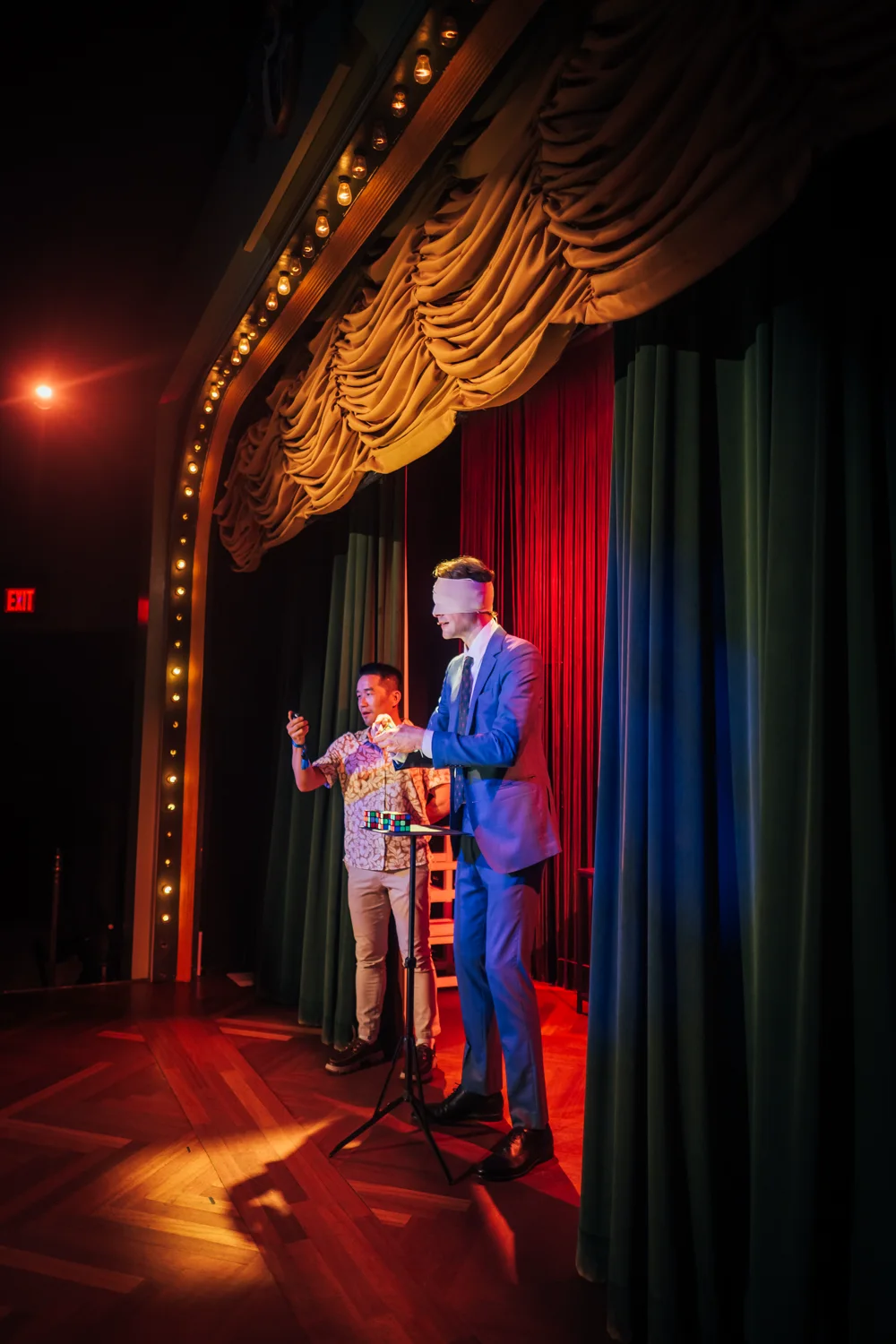 Blindfolded Kevin Blake performing with a guest beneath the Palace’s illuminated proscenium