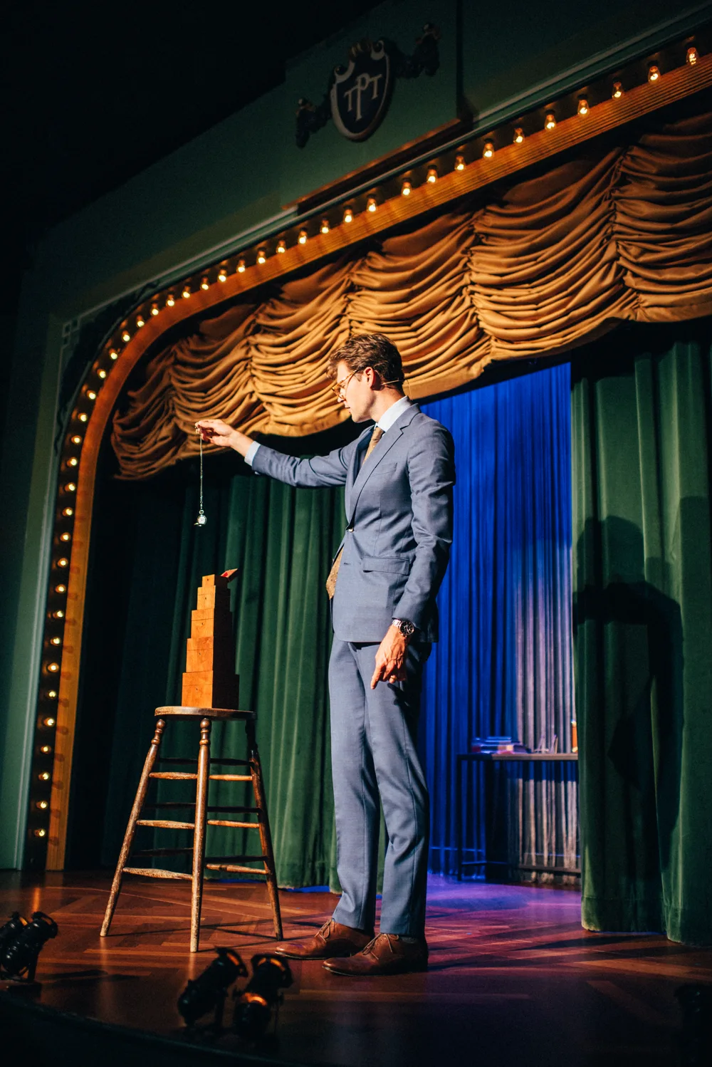Kevin Blake holding a pocket watch above a stack of wooden blocks on the Palace stage